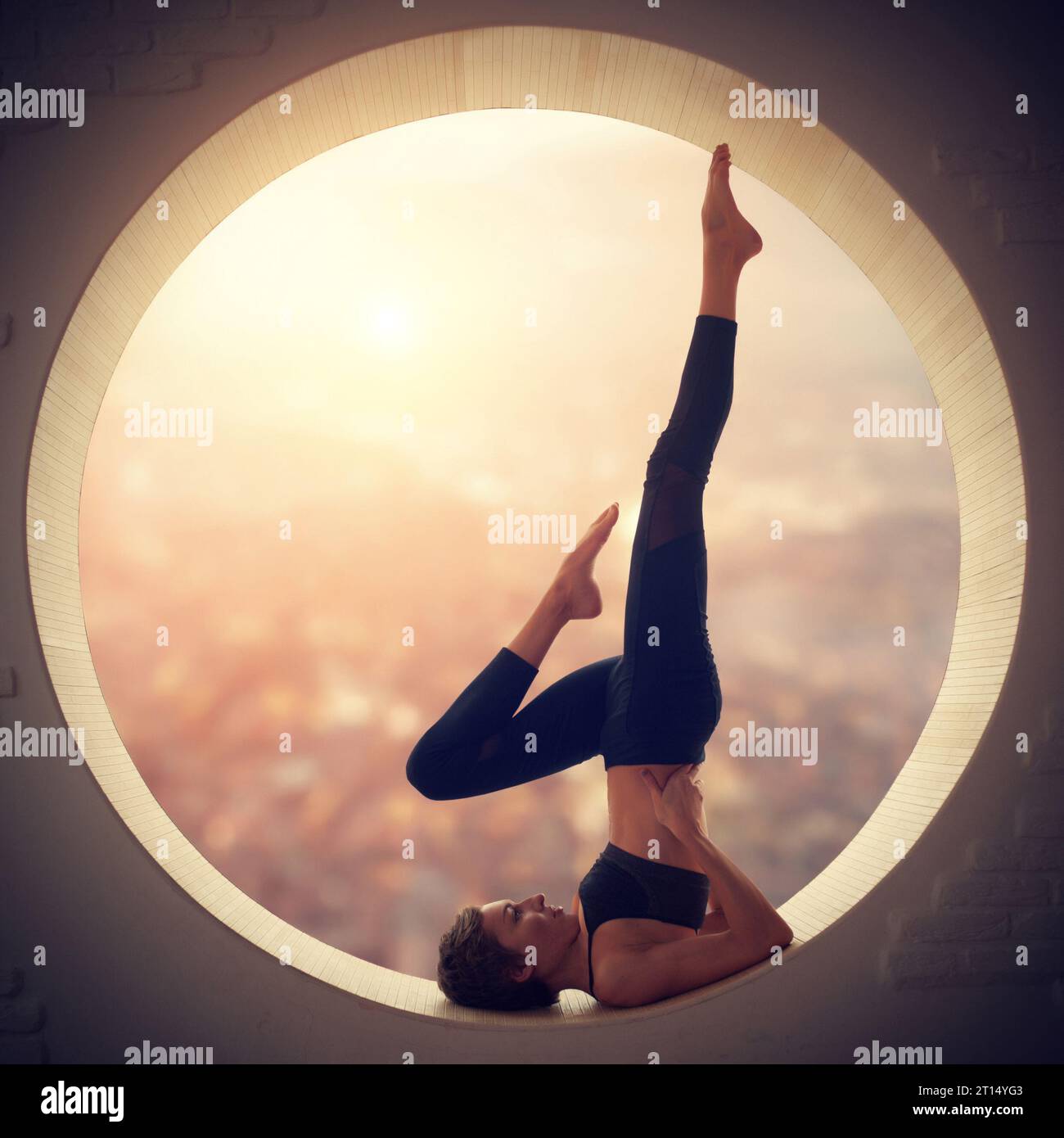 Beautiful sporty fit yogi woman practices yoga handstand asana Salamba Sarvangasana - shoulderstand pose in a round window with arial view of the city Stock Photo