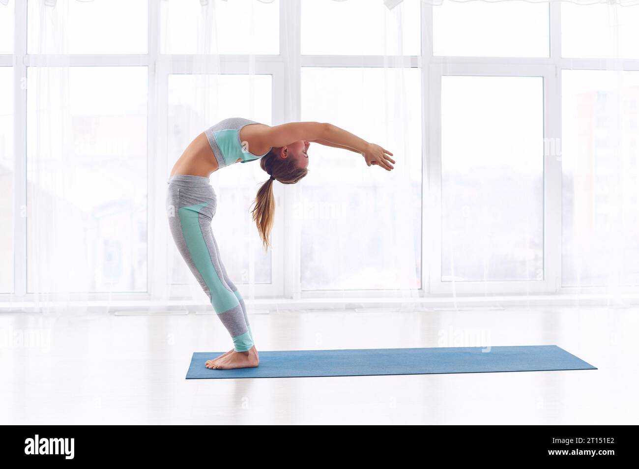 Beautiful young woman practices yoga asana Ardha Chakrasana - half wheel pose at the bright yoga class with large windows Stock Photo