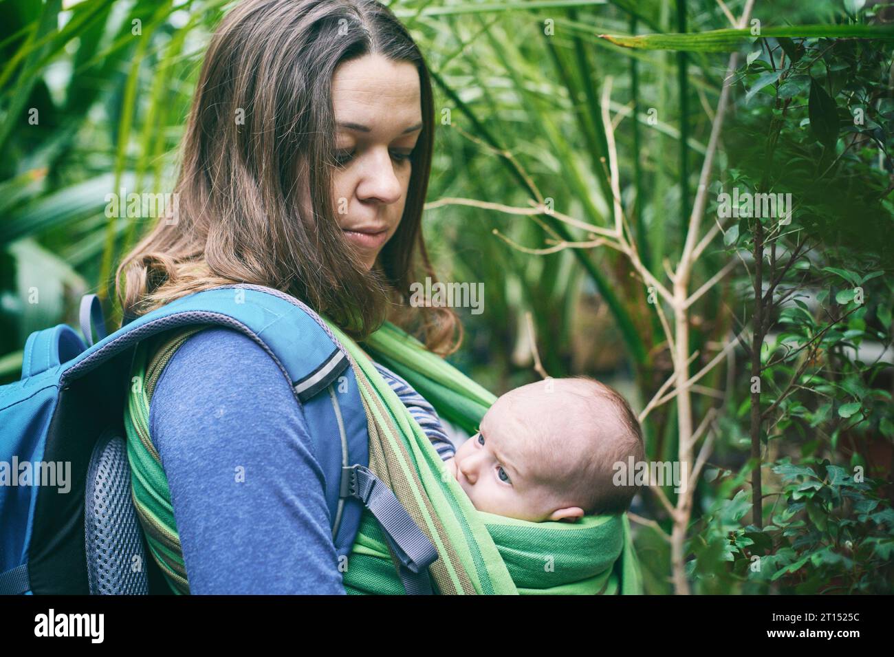 A young mother with a baby in a sling is walking in the tropical forest