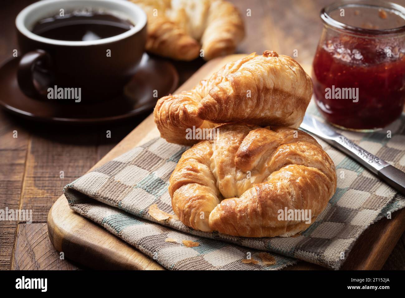 Two croissants with strawberry preserves and cup of coffee on rustic wooden table Stock Photo