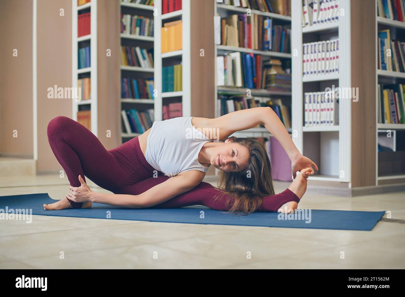 Beautiful woman practices yoga asana Parivrtta Janu Sirsasana - breakdown pose in the library. Stock Photo