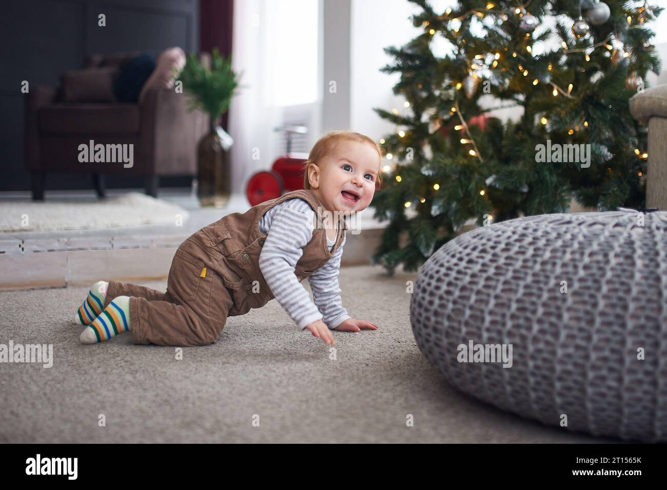 1 year old baby boy crawling on floor at home. christmas decorations on a background. Stock Photo