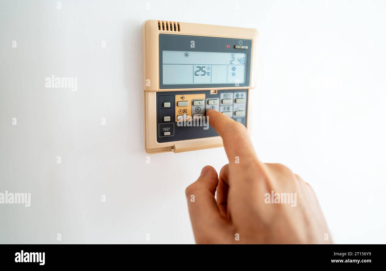Man's hand adjusting wall-mounted digital thermostat. Stock Photo