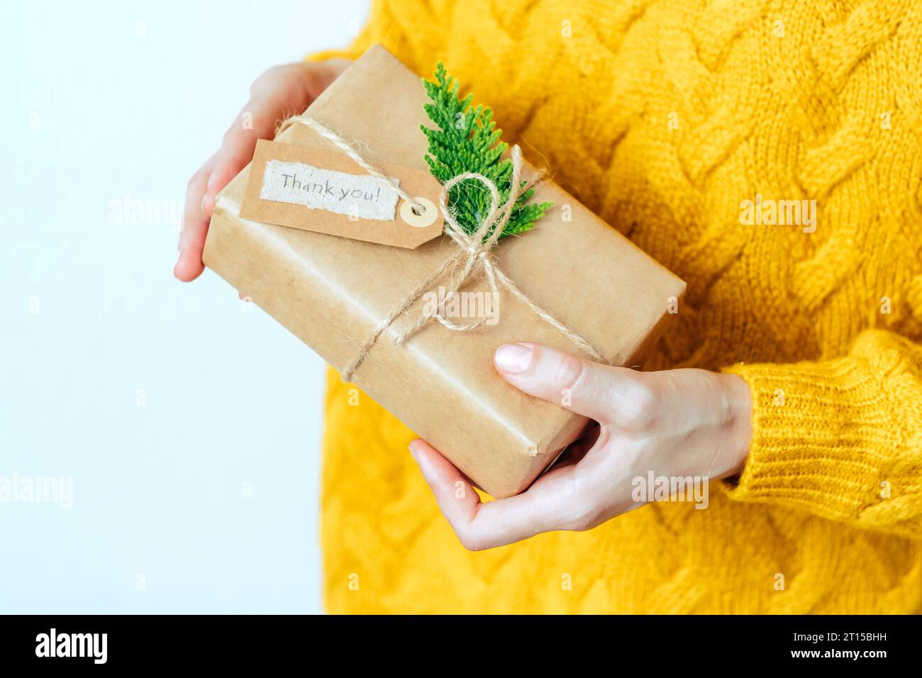 An unrecognizable woman in yellow sweater with eco friendly gift box with tag with the words thank you. Sustainable and eco conscious living concept Stock Photo