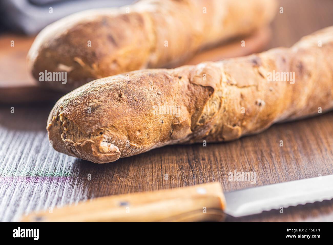 Wholegrain rustical baguette on the wooden table. Stock Photo