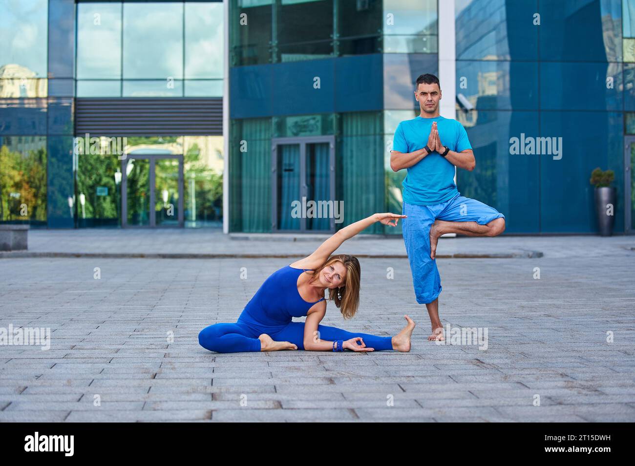 An attractive young woman and man doing yoga outdoors against the background of a modern city. Stock Photo