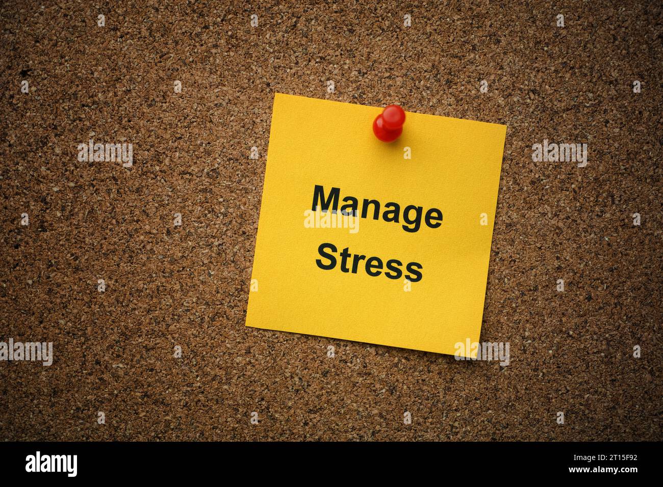 A yellow paper note with the words Manage Stress on it pinned to a cork board. Close up. Stock Photo