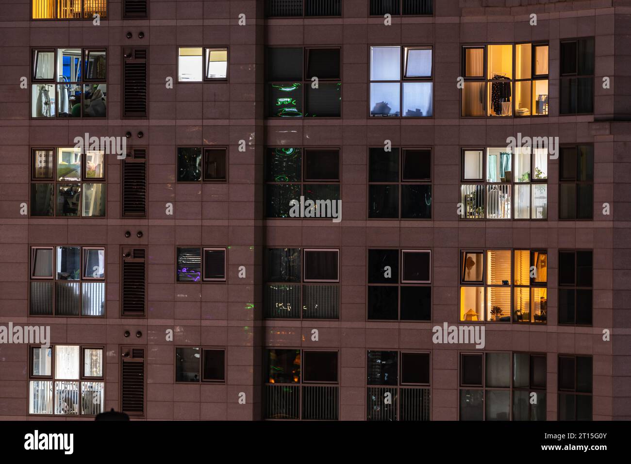 An apartment where houses with the same spatial structure are stacked like tiles. After sunset, lights turn on in the windows, showing different color Stock Photo