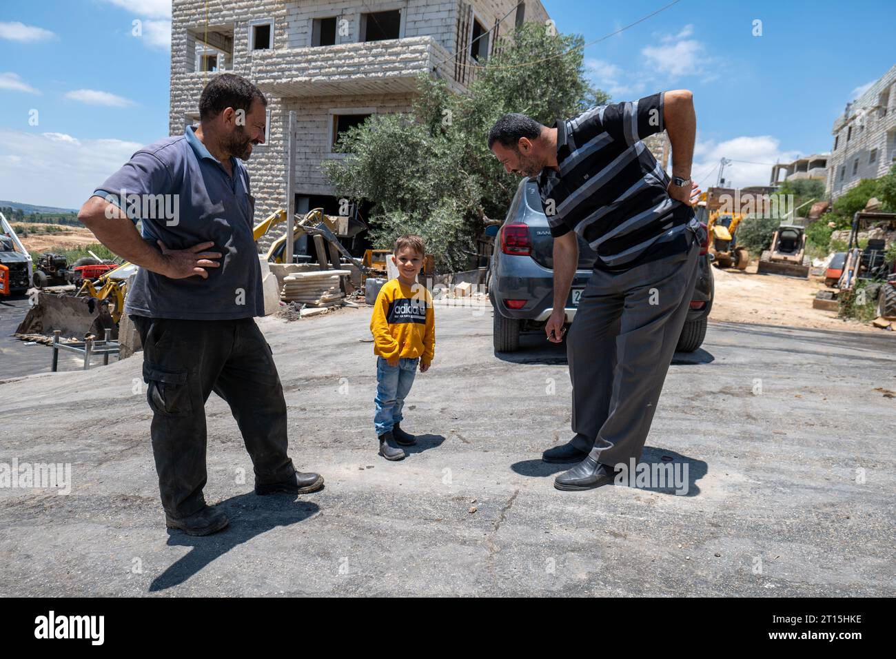 Bayt Surik, Palestine – June 19, 2023: Happy Arab Male Entrepreneurs Stand with a Young Smiling Boy in Yellow Shirt by a White Stone House Stock Photo