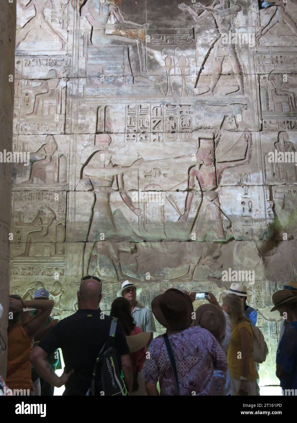 Tourists stand in front of the fine carvings & decorative reliefs in the Great Temple of Abydos, from the time of Seti I & dedicated to the god Osiris. Stock Photo