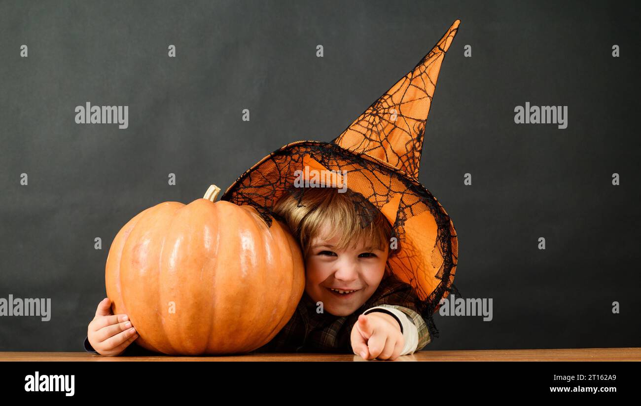 Happy Halloween. Smiling child with pumpkin for Halloween. Little boy in witch hat with jack-o-lantern pointing to you. Trick or treat. Preparation Stock Photo
