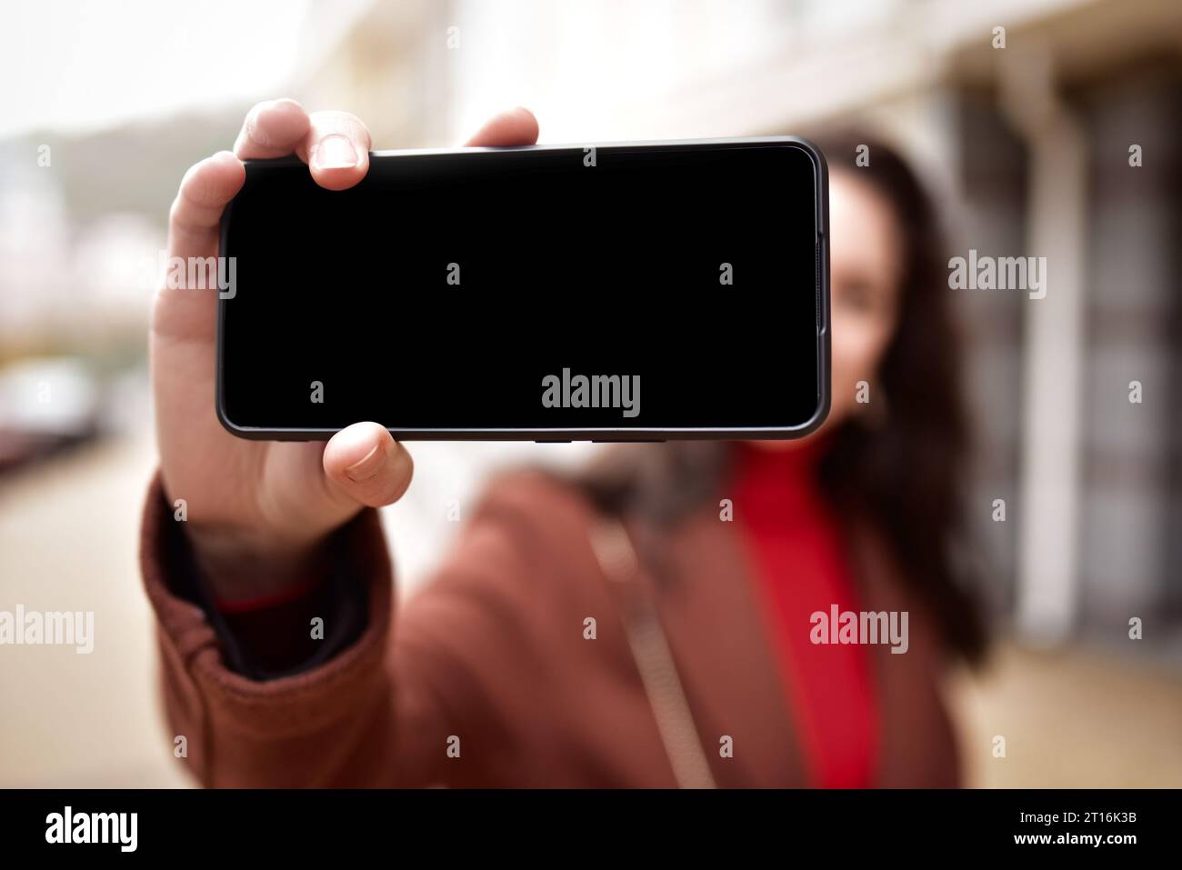 young woman taking selfies walking down the street, holding a smartphone with a black screen. copy space.blank screen Stock Photo