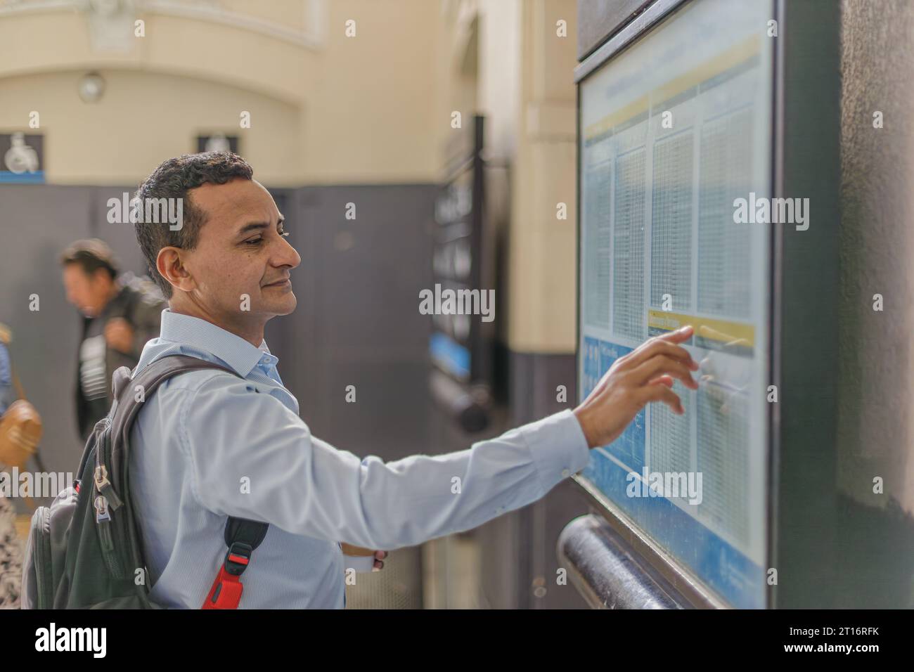Latin man in shirt looking at billboard with train schedules. Stock Photo