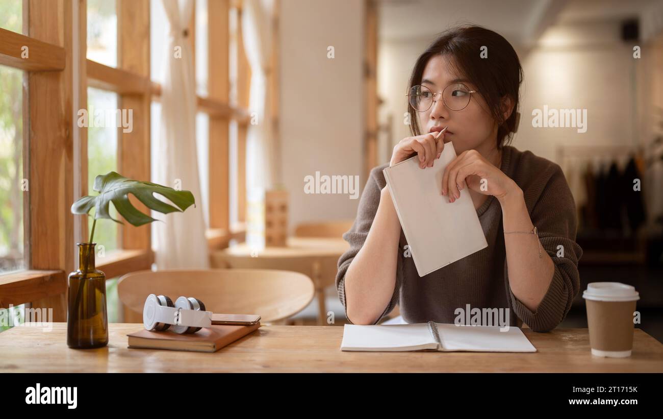 A pensive, thoughtful young Asian woman sits at a table in a beautiful ...