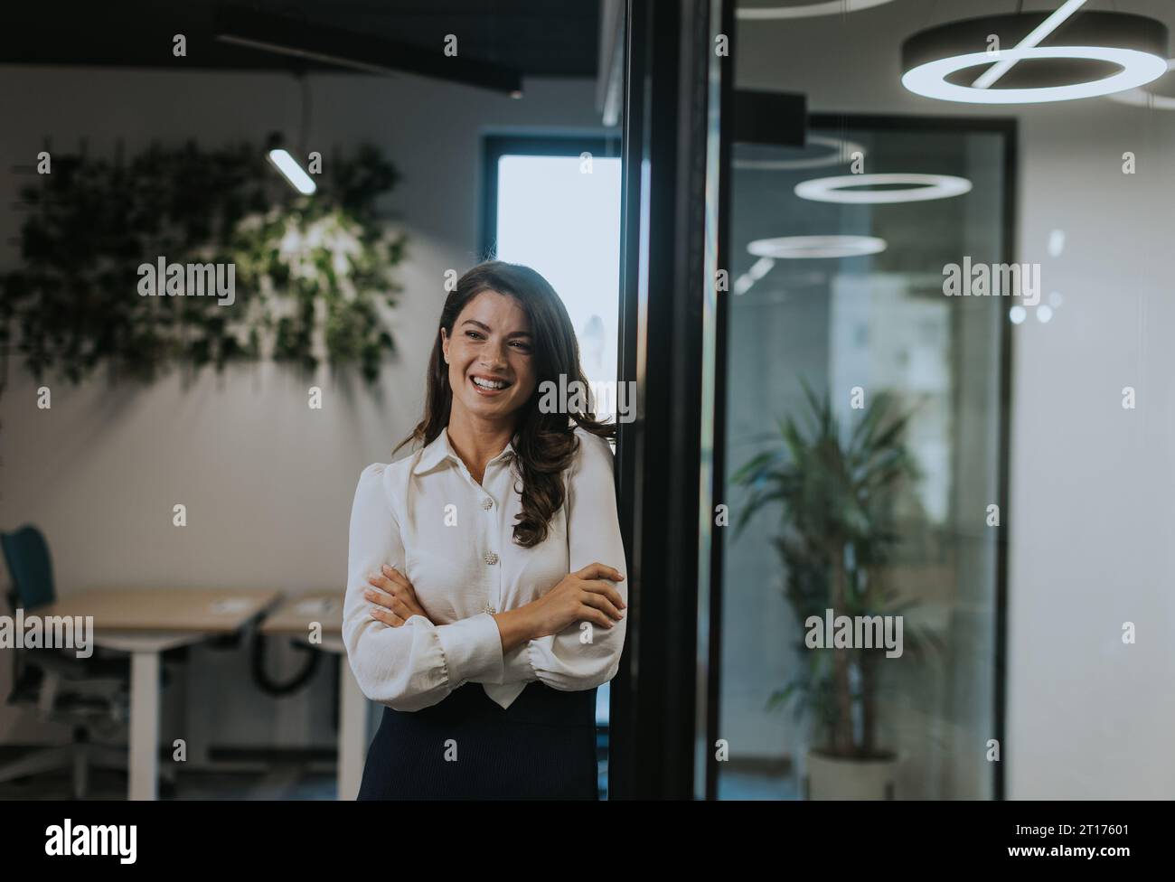 Pretty young business woman standing with arms crossed in the modern ...