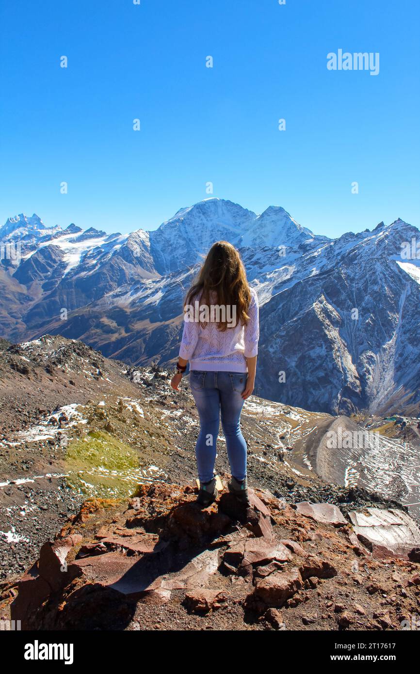 The girl with her back to the camera looking at the tall mountains in ...
