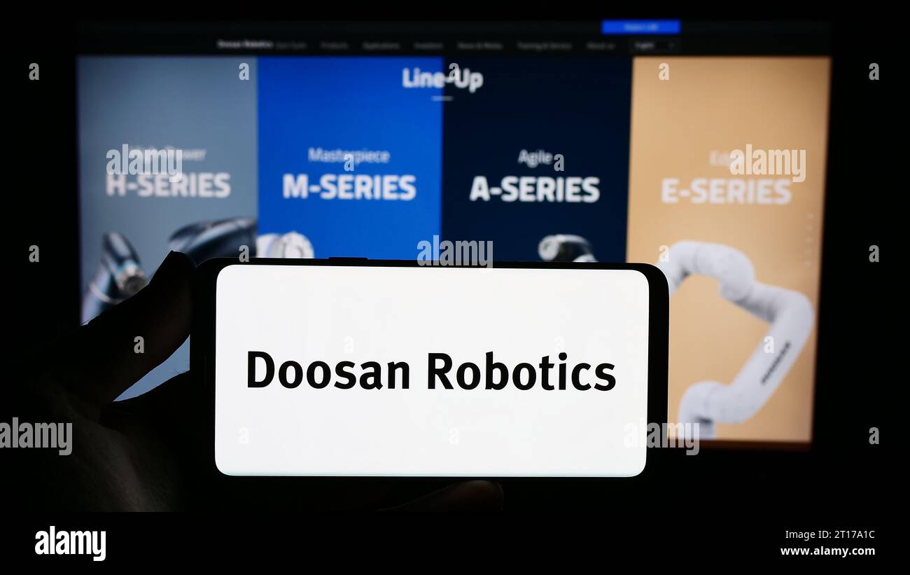 Person holding smartphone with logo of Korean robot company Doosan Robotics Inc. in front of website. Focus on phone display. Stock Photo