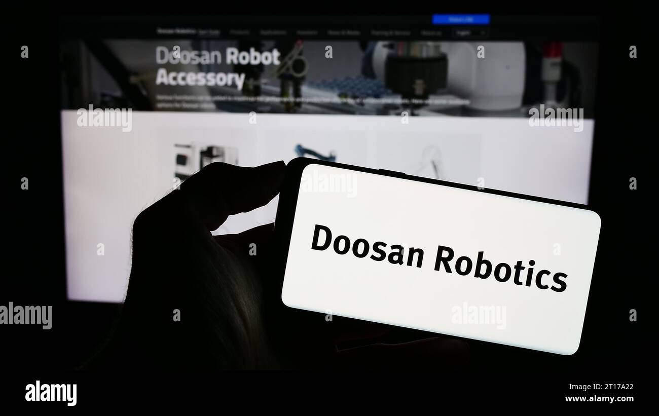 Person holding cellphone with logo of Korean robot company Doosan Robotics Inc. in front of business webpage. Focus on phone display. Stock Photo