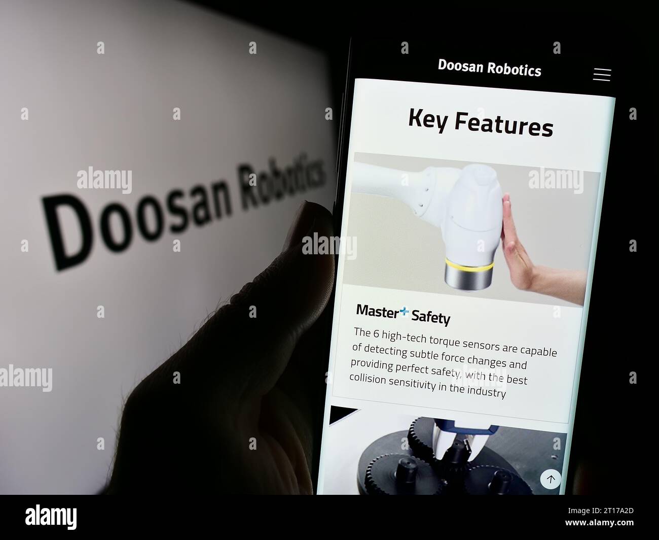 Person holding cellphone with website of Korean robot company Doosan Robotics Inc. in front of business logo. Focus on center of phone display. Stock Photo