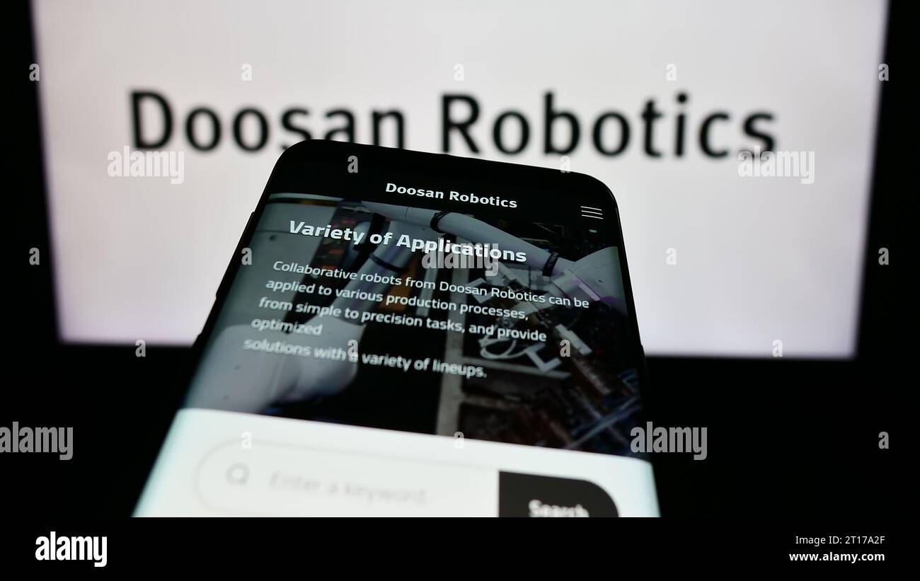 Mobile phone with website of Korean robot company Doosan Robotics Inc. in front of business logo. Focus on top-left of phone display. Stock Photo