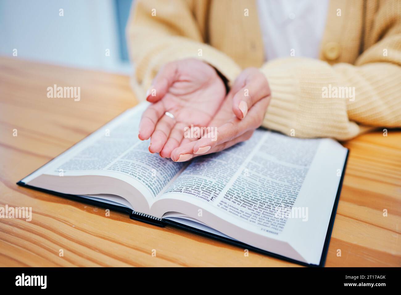 Hands, bible and prayer at desk, religion and Christian worship in home at table. Closeup, holy book and woman in meditation for God, Jesus and Christ Stock Photo