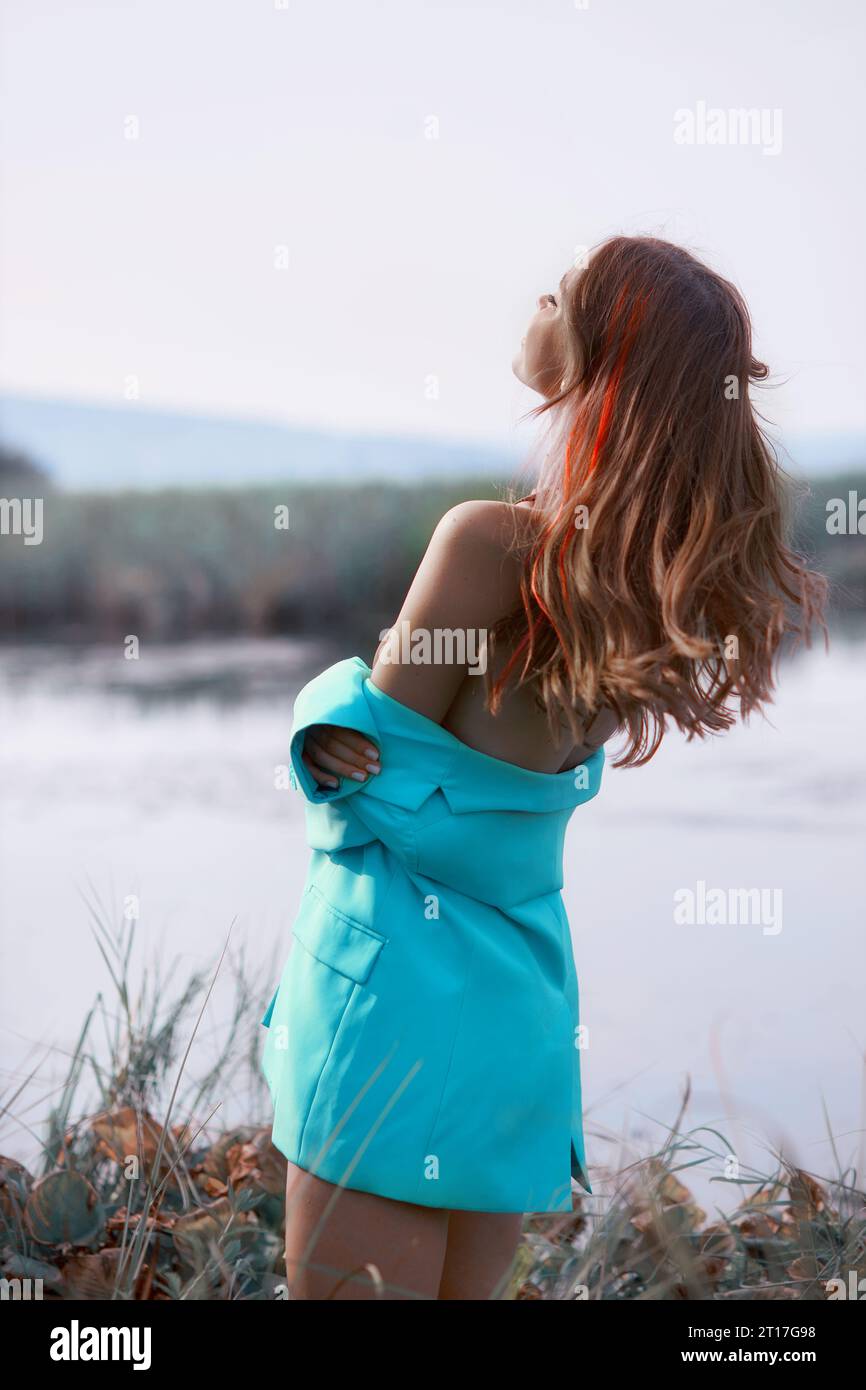 Beautiful woman walking by the lake, blue jacket and red dyed hair Stock Photo