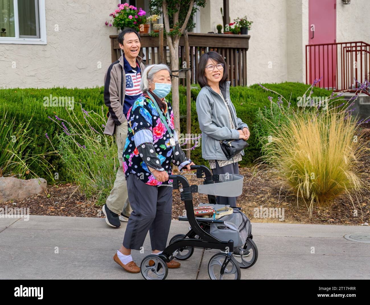 Senior woman walking with mobility walker. Family laughing and walking outside the retirement village. California. Stock Photo