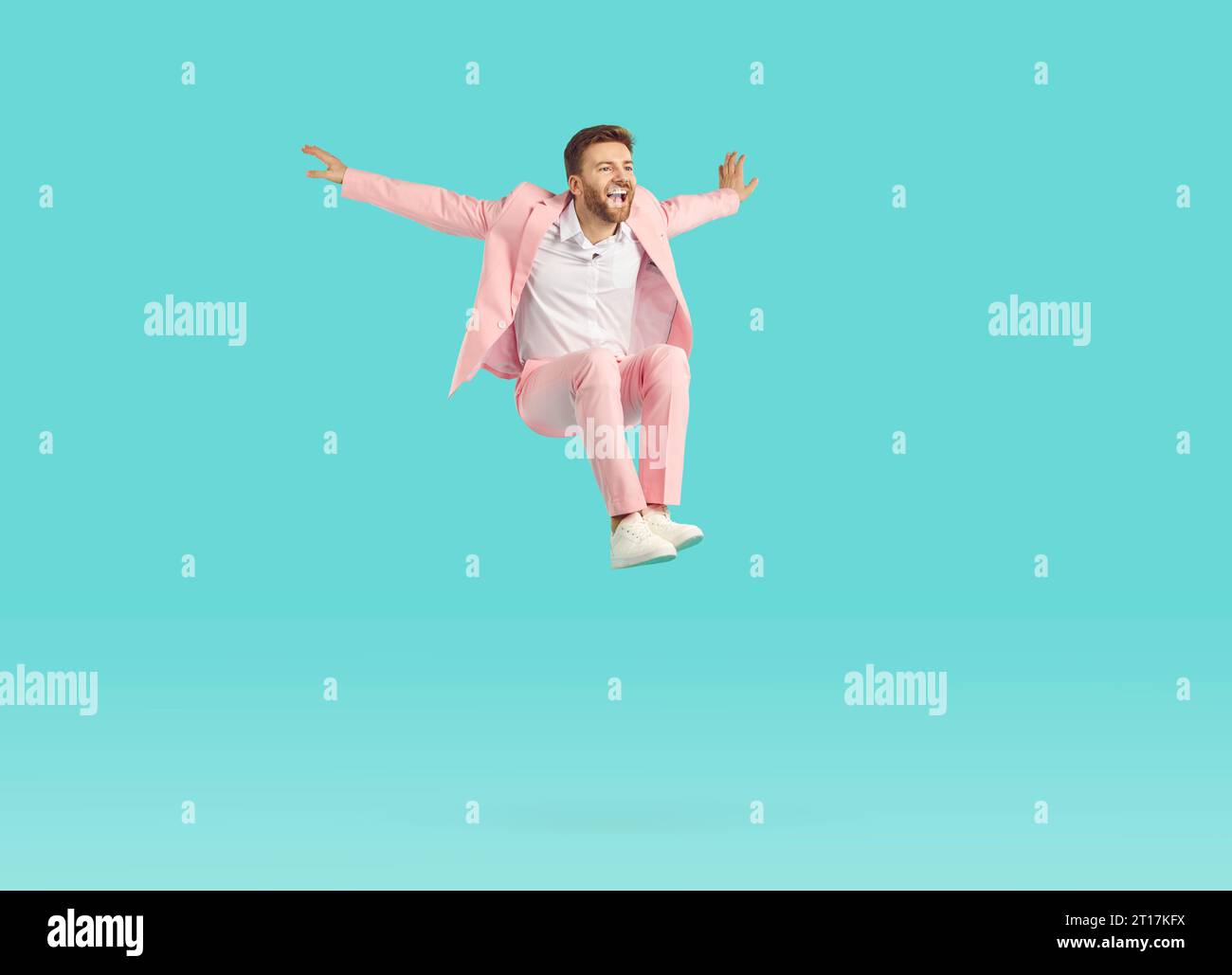 Funny excited man wearing stylish pink suit jumping isolated on studio blue background. Stock Photo