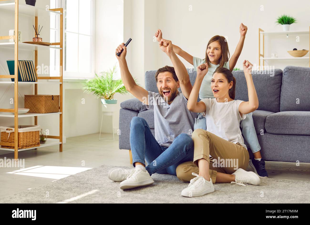 Happy mom, dad and child watching football match on TV, celebrating goal and cheering Stock Photo
