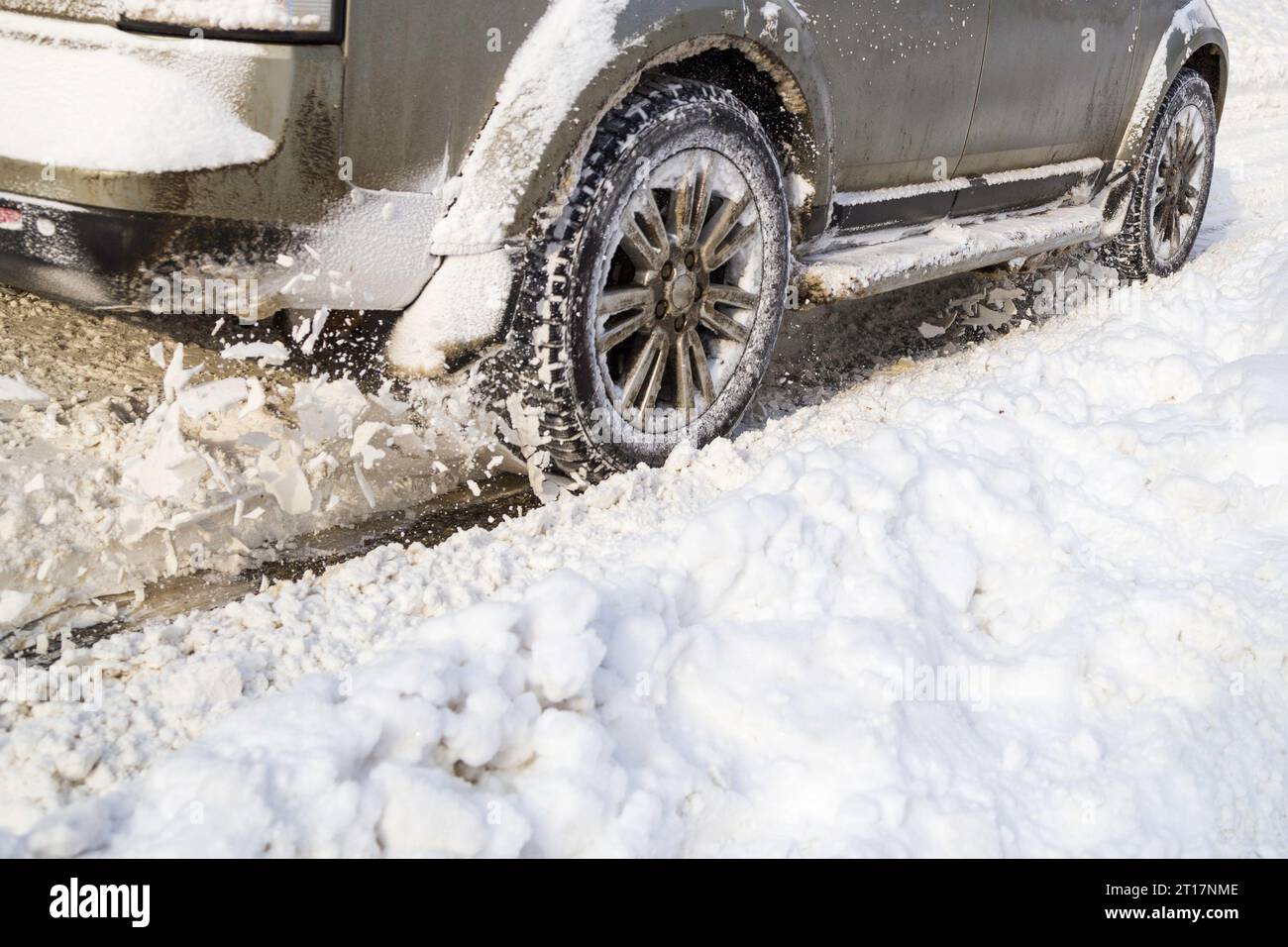 Road snow flies up from a vehicle's spinning wheel. Car's wheels spin