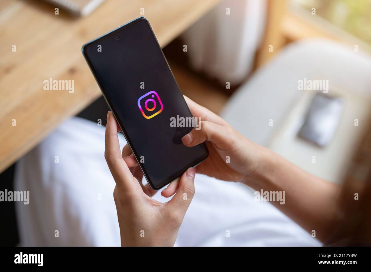 Chiang mai, Thailand - Oct 12 2023: A woman is using Instagram on her smartphone while relaxing in a cafe. Instagram logo on an iPhone 14. Social medi Stock Photo