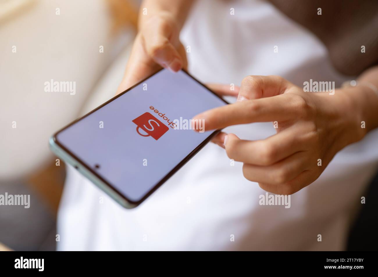 Chiang mai, Thailand - Oct 12 2023: A woman is using Shopee on her smartphone while relaxing in a cafe. Shopee logo on an iPhone 14. Online shopping, Stock Photo