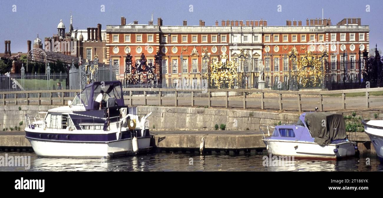 Archival 1997 view of Hampton Court Palace from River Thames small boats at moorings beside Jean Tijou ornate gilded screen gates and fence with Sir Christopher Wren building of the south front facade beyond in  Richmond London England UK Stock Photo