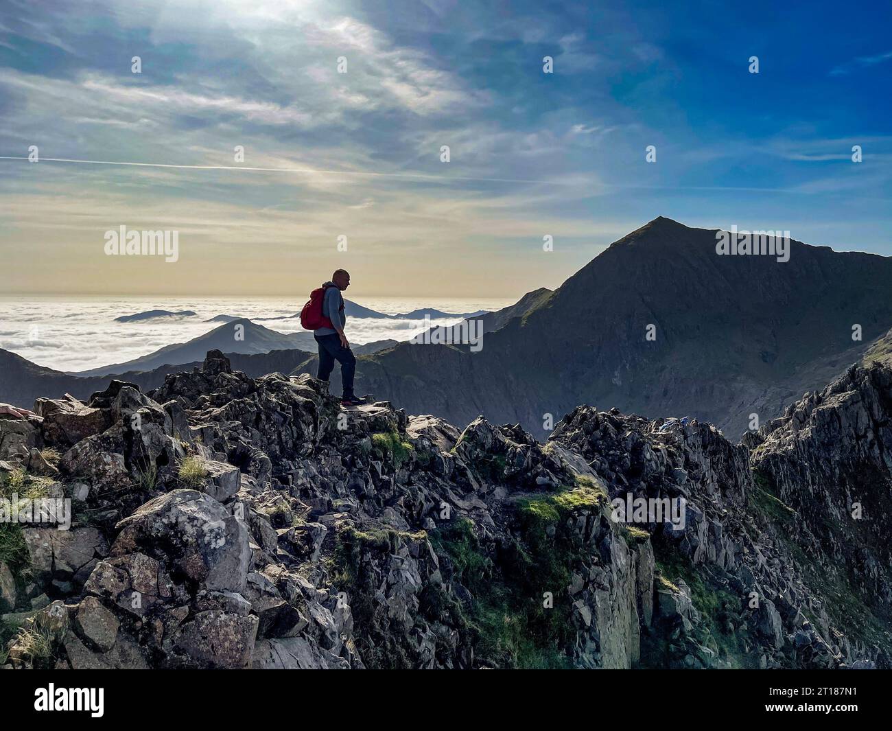 Lone climber on Crib Goch with Cri-y-ddysgl and Mount Snowdon in the distance, with low clouds filling the valley behind. Wales. UK Stock Photo