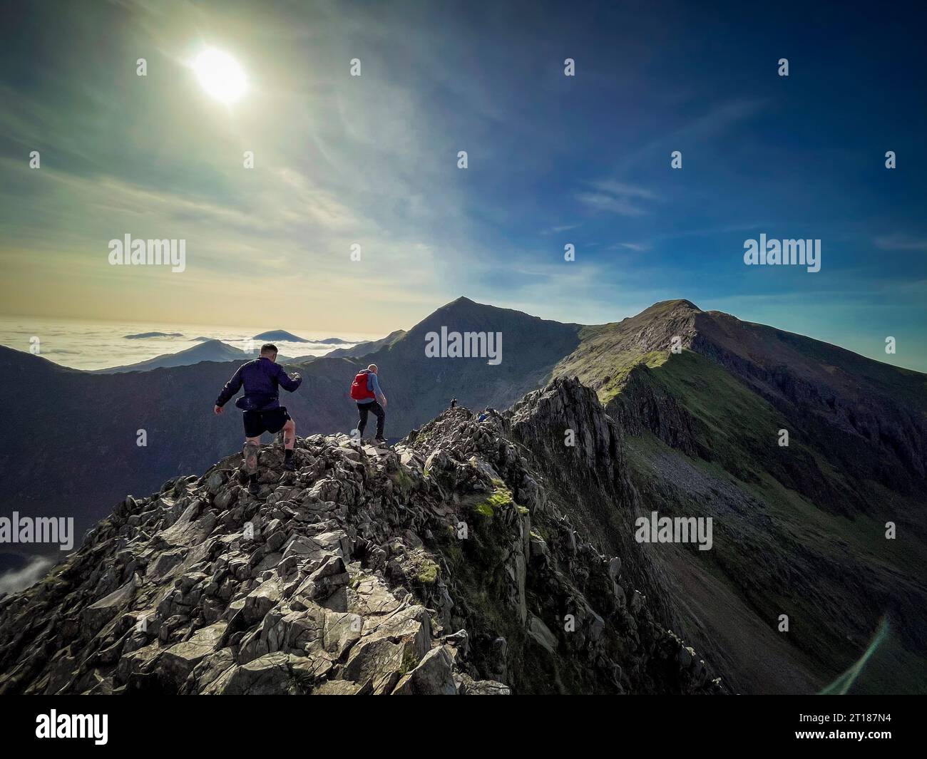 Male climbers on the challenging Crib Goch with Cri-y-ddysgl and Snowdon in the distance on a sunny Autumn day. Wales. UK. Stock Photo