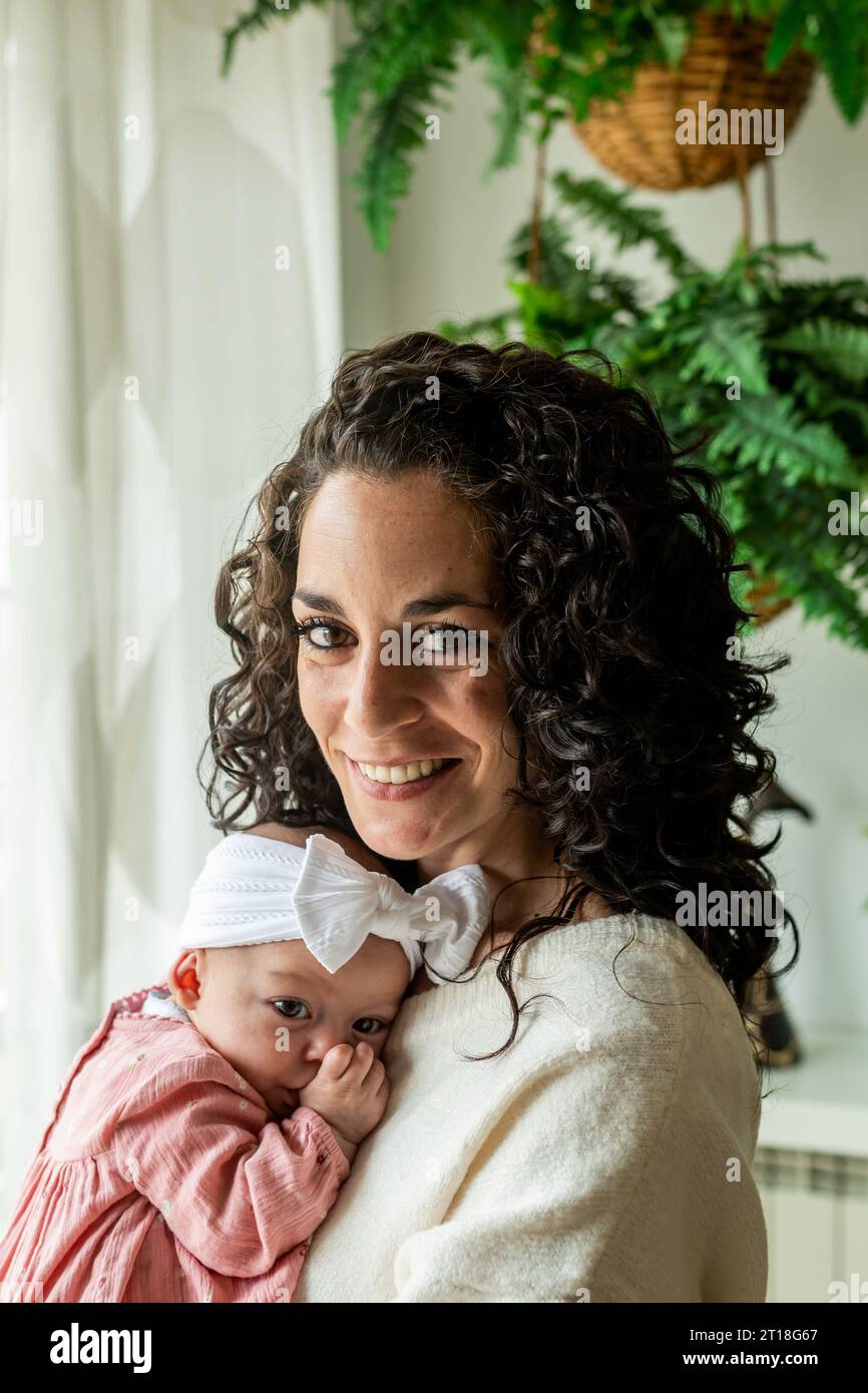 young brunette mother with curly hair holds her little baby in her arms while sucking her thumb to fall asleep. secure attachment and respectful paren Stock Photo