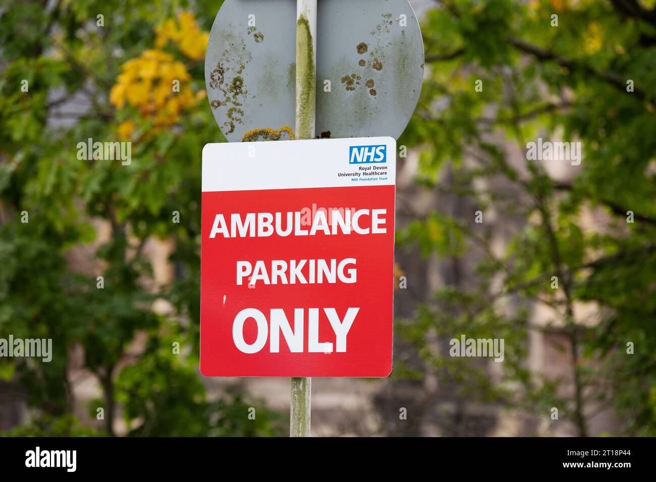 Ambulance parking ONLY red NHS sign on pole with blurred tree branches in background Stock Photo