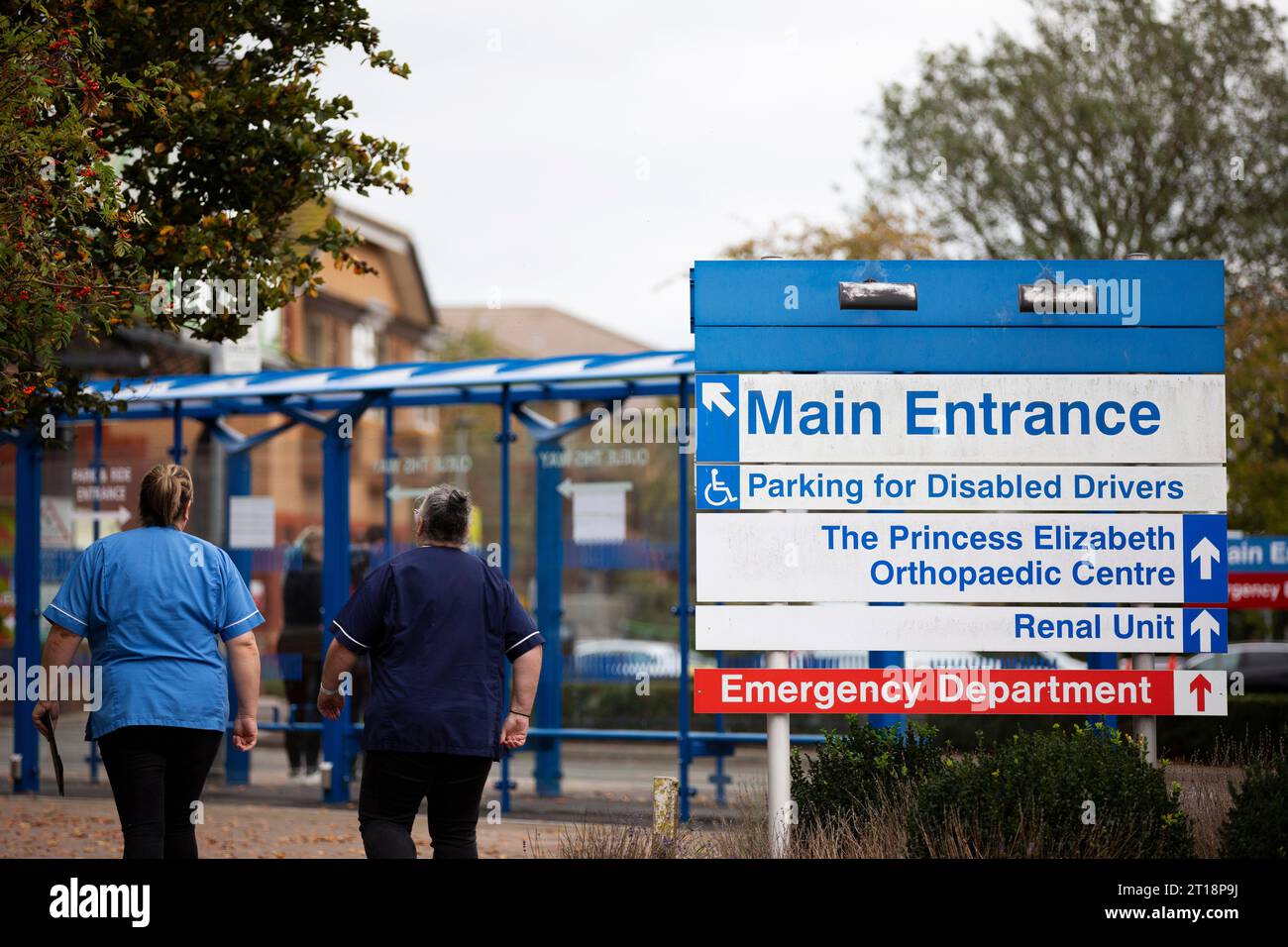 back view of NHS hospital staff in blue uniform walking towards main entrance at Exeter R D & E hospital Devon Stock Photo