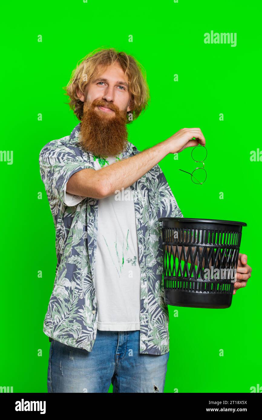 Redhead man taking off throwing out glasses into bin after medical vision laser treatment therapy surgery looking smiling at camera, heal, cure. Handsome guy isolated on green chroma key background Stock Photo