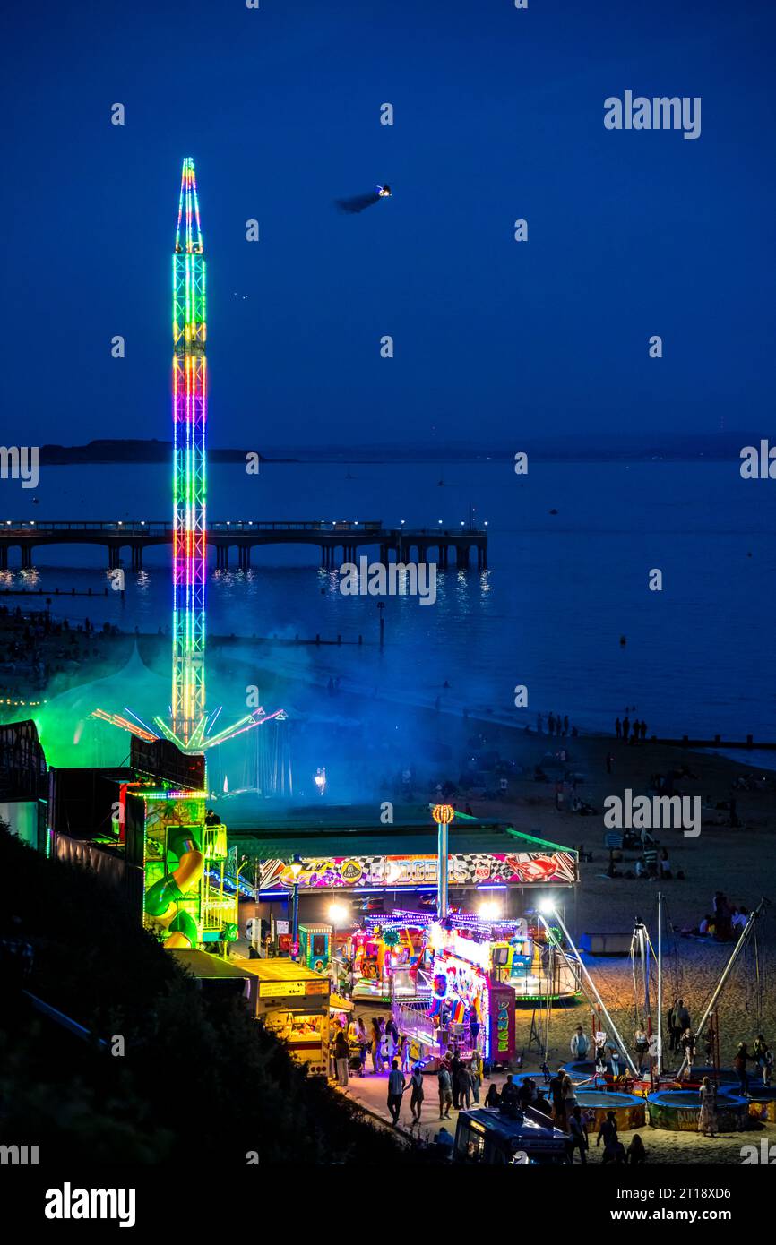 Otto the Helicopter making an entrance from the east seen next to the fairground rides on Boscombe beach in the evening at the 2023 Bournemouth Air Fe Stock Photo
