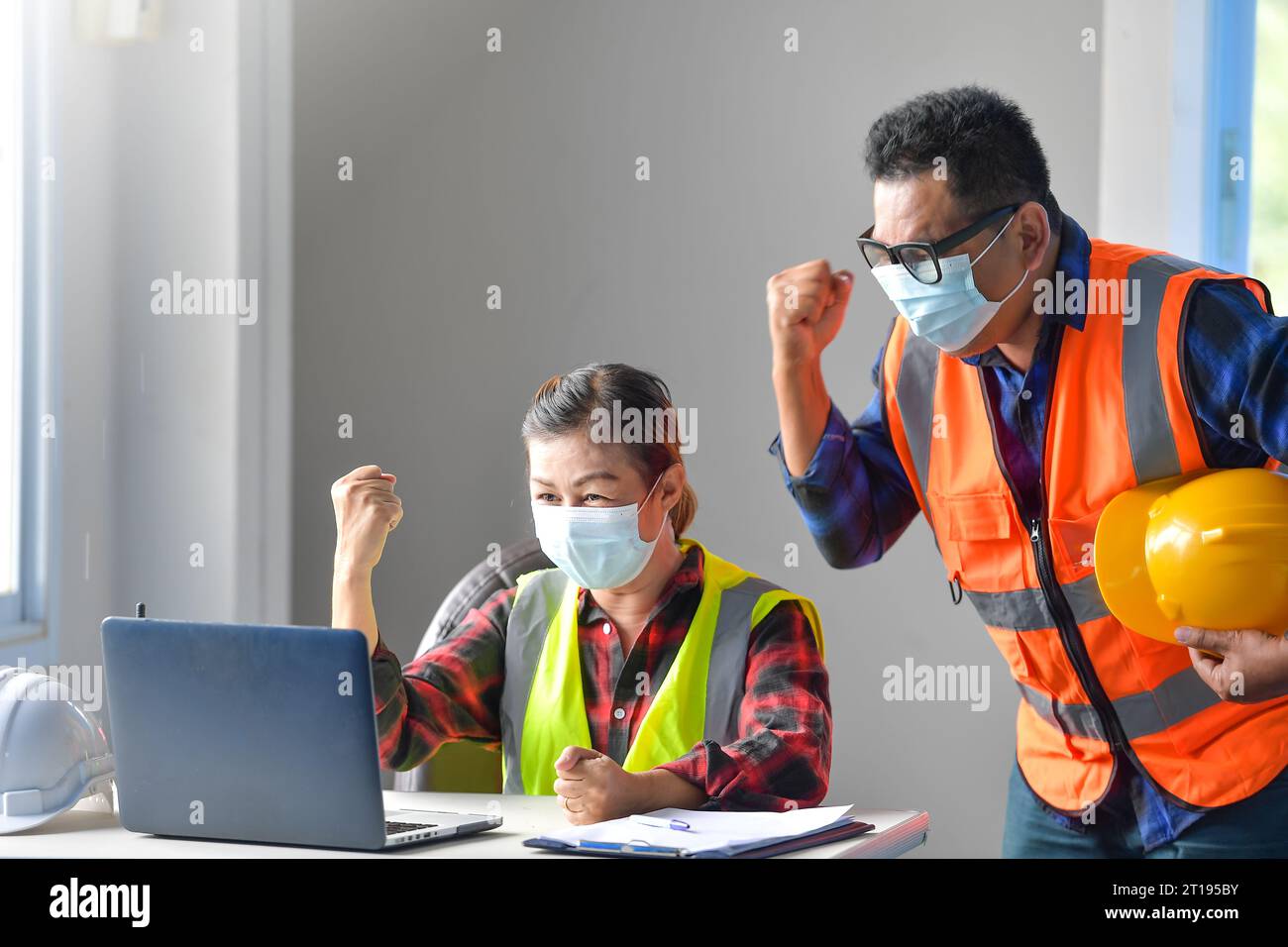 Two excited building inspectors in an office on a video call punching the air Stock Photo