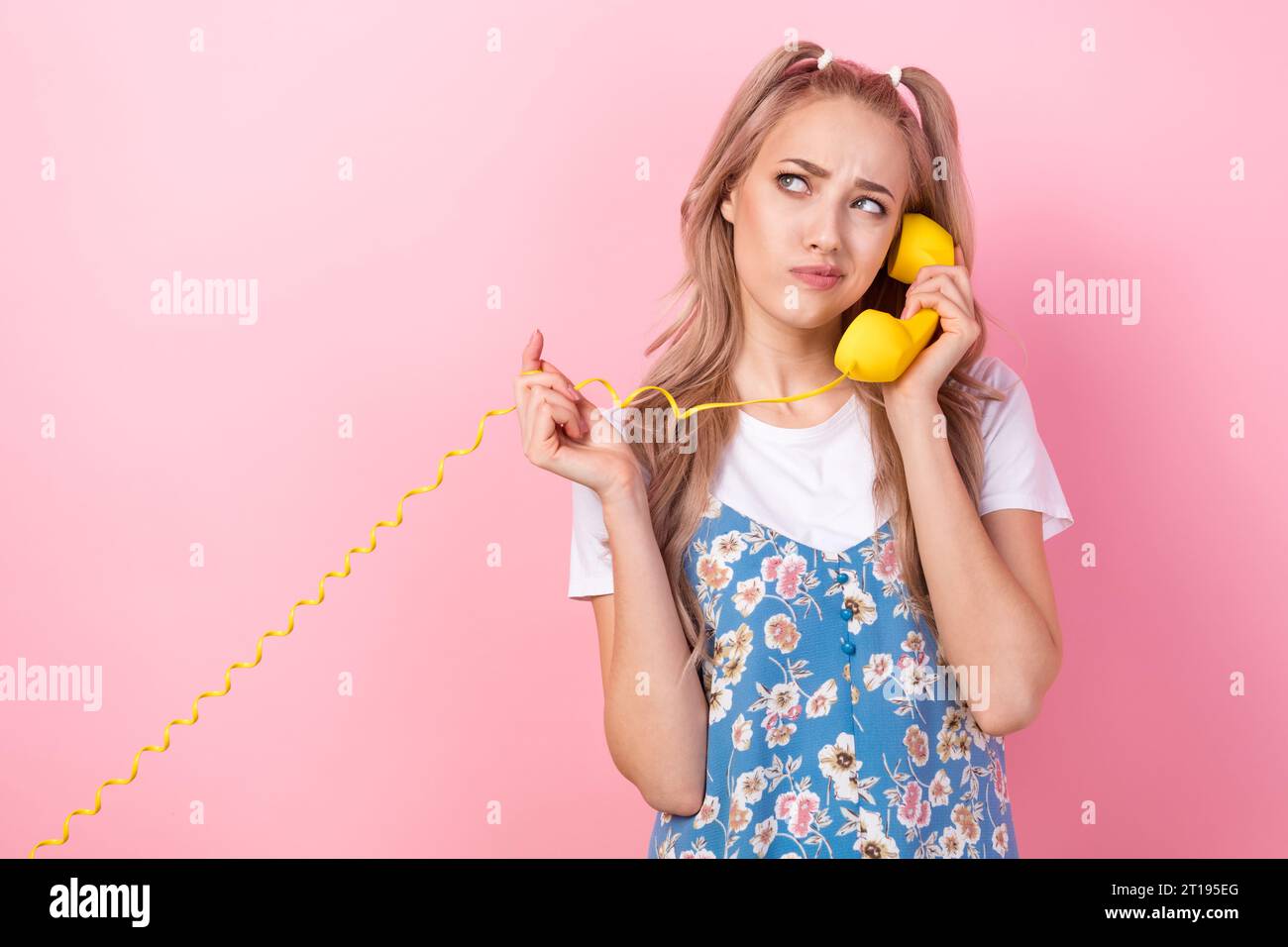 Portrait of minded girl with tails wear t-shirt under dress talk on phone look empty space hold cable isolated on pink color background Stock Photo