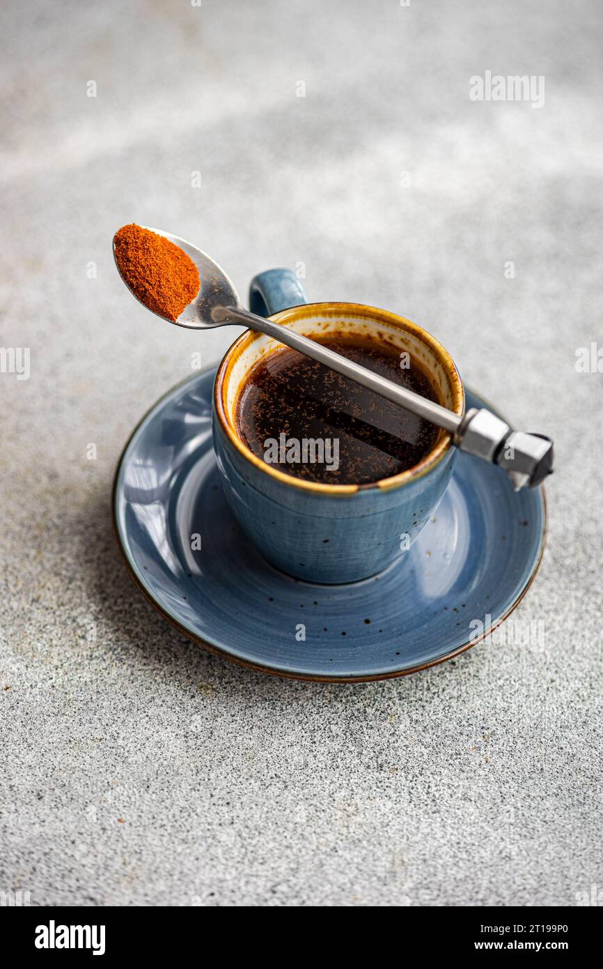 Overhead view of a cup of black coffee with a spoonful of ground paprika Stock Photo