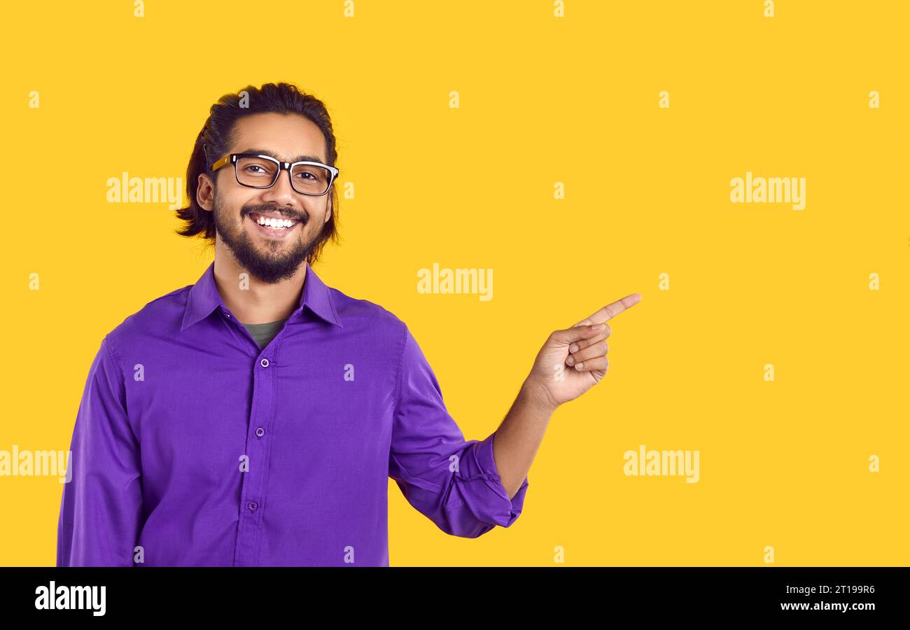 Happy Indian man standing on yellow color background and pointing to side at copy space Stock Photo