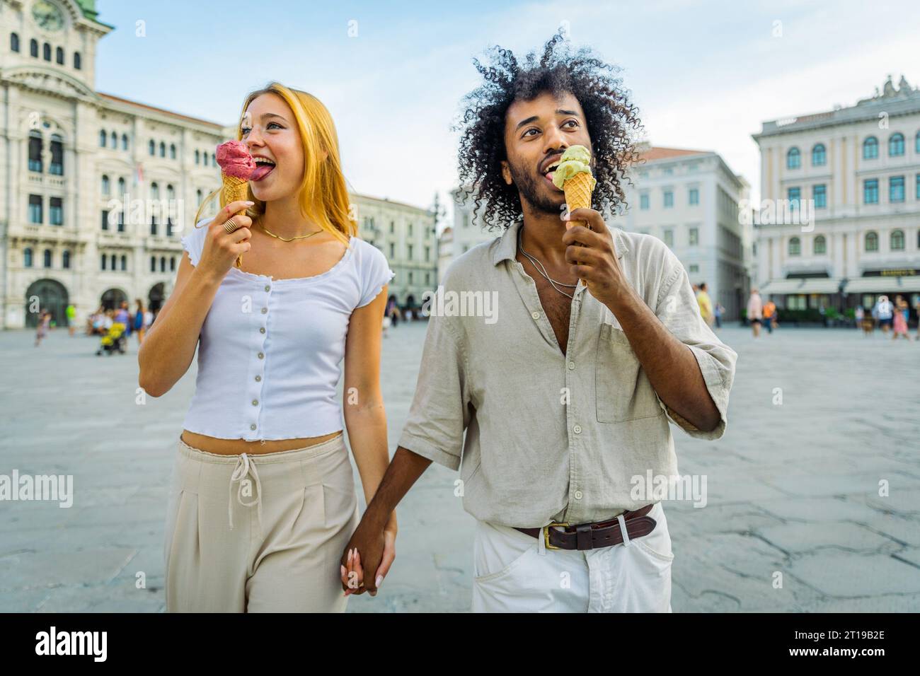 Two lovers hold hands while eating ice cream together in the city center. Stock Photo