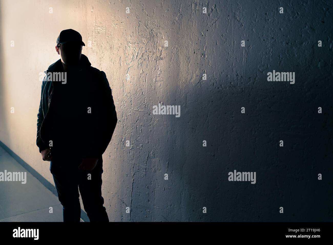 Suspicious man. Silhouette of criminal. Stalker or anonymous stranger. Gang crime, teenage gangster or thief. Dark urban street alley. Face hidden. Stock Photo