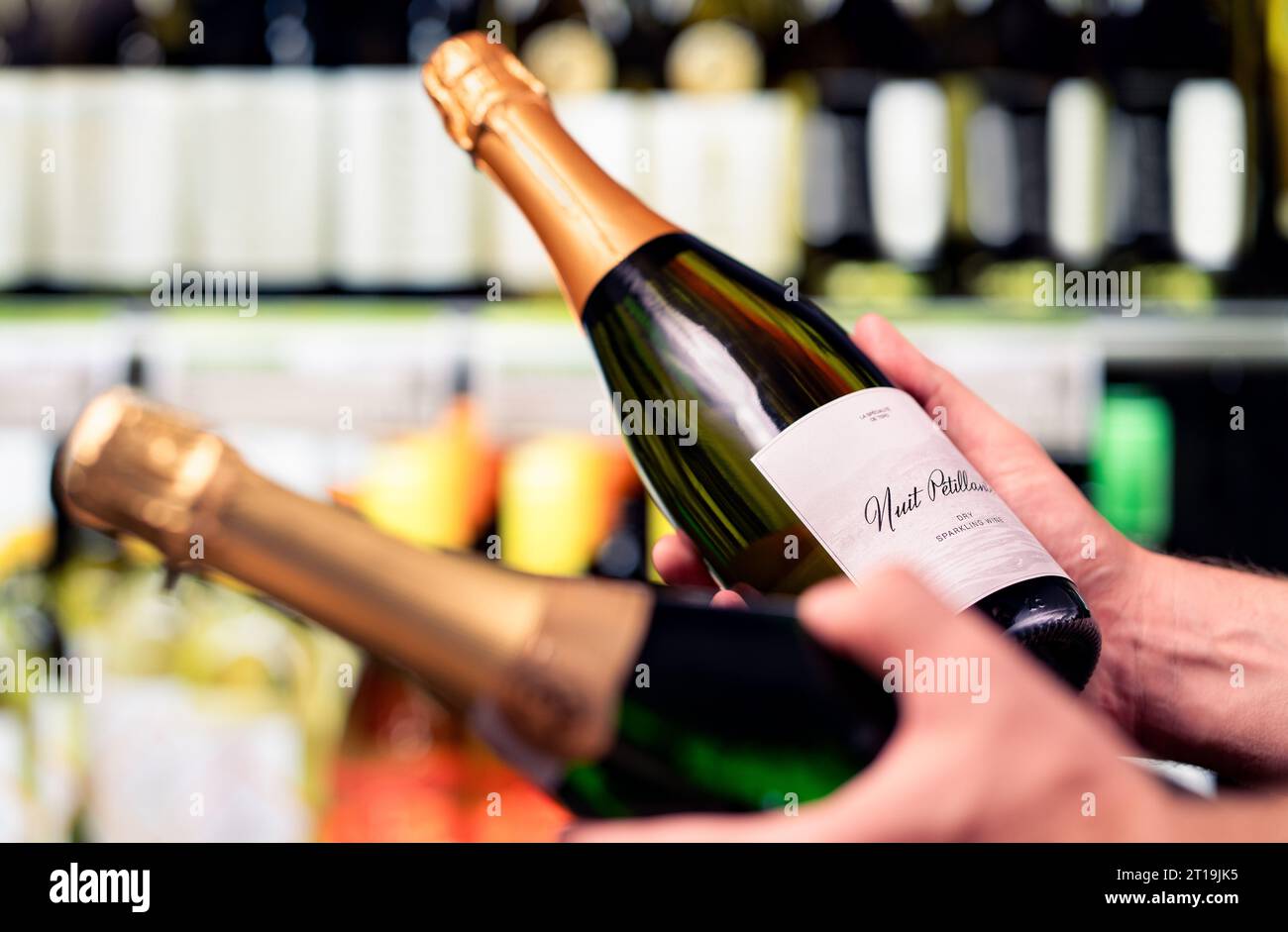 Sparkling wine in alcohol store. Champagne or prosecco in liquor shop. Man holding two bottles in hands, choosing drink. Stock Photo