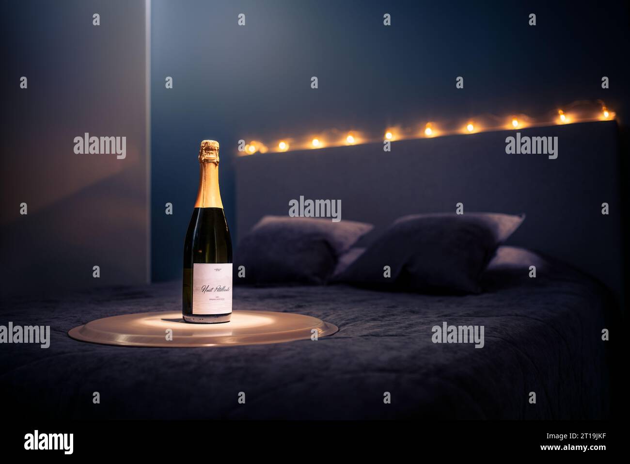 Champagne bottle on hotel room bed. Sparkling wine. Romantic couple date night, anniversary celebration or surprise on special day. Beautiful lights. Stock Photo