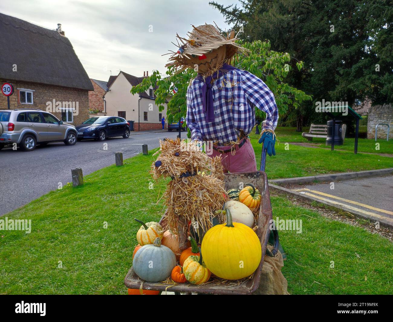 Gardener scarecrow with wheelbarrow containing dog and pumpkins at scarecrow festival on Sharnbrook village green, Bedfordshire, England, UK Stock Photo