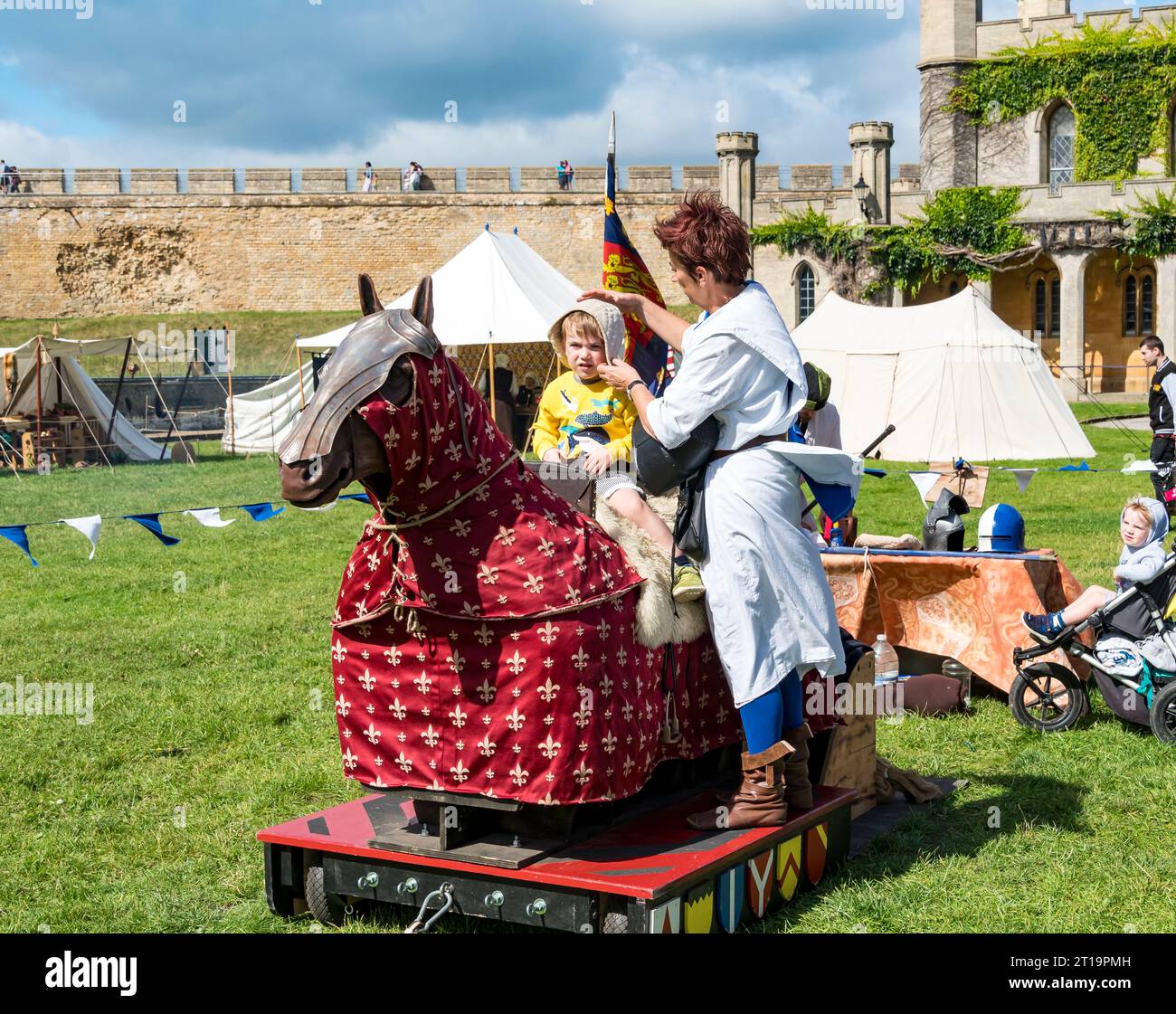 Lady helper putting padded scull cap on small boy sitting on practice jousting horse, Lincoln castle, Lincoln City, Lincolnshire, England, UK, Stock Photo